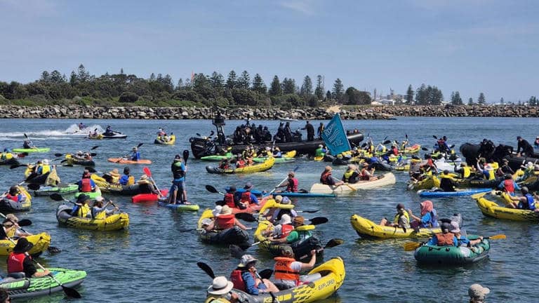 Protesters in kayaks block the shipping channel at Newcastle Port during a climate protest, with police officers in inflatable boats making arrests.